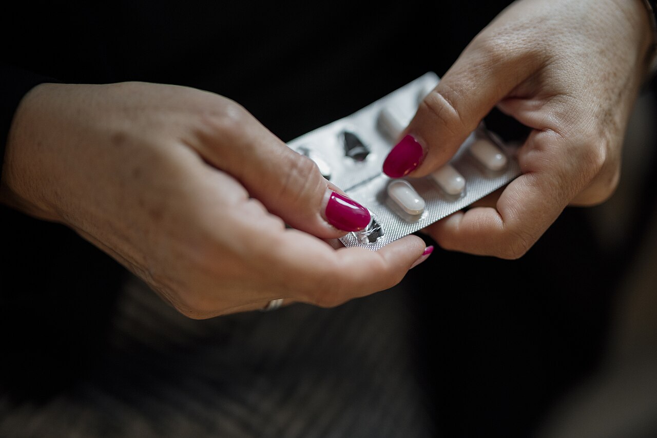 A person uses both hands to carefully open a pack containing pills. The focus is on the action of taking the medication. The setting appears to be a l