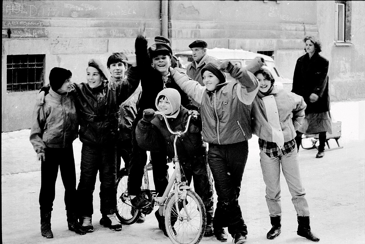 Sarajevo siege life, winter of 1992-1993. The children's spontaneous joy in a fresh snowfall contrasts with the anxiety on the faces of the adults wal